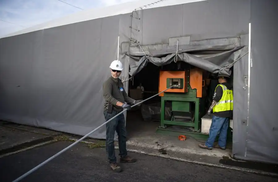 Investment Recovery Center foreman David Boggs, left, and material handler Beau Benavides, right, feed old transmission cable into a SWEED cable chopper